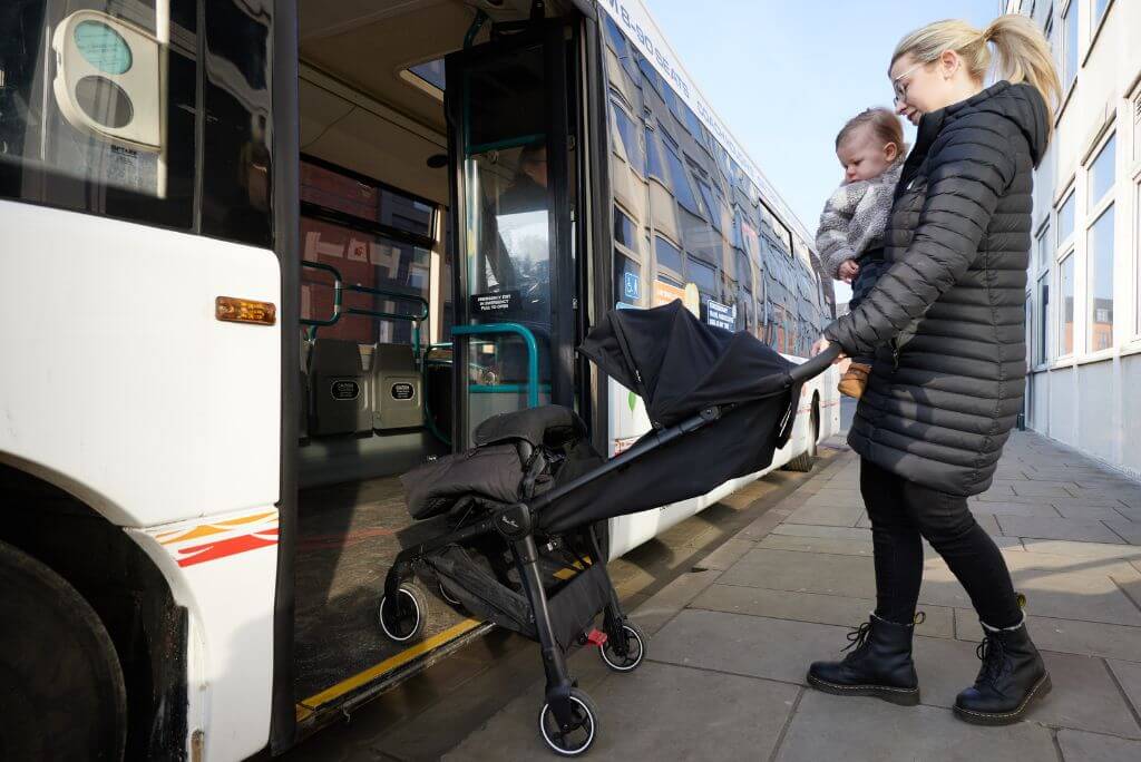Lady pushing a pram onto a bus whilst holding toddler