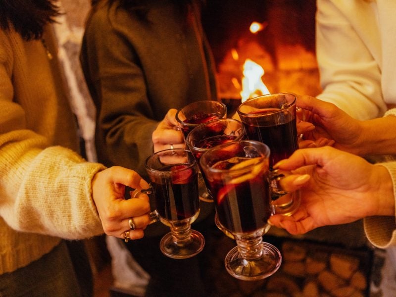 Close-up of the women saying a toast and clinking glasses with mulled wine. Cups of spicy hot Christmas drink at a house party. New Year Eve. Meeting family and friends